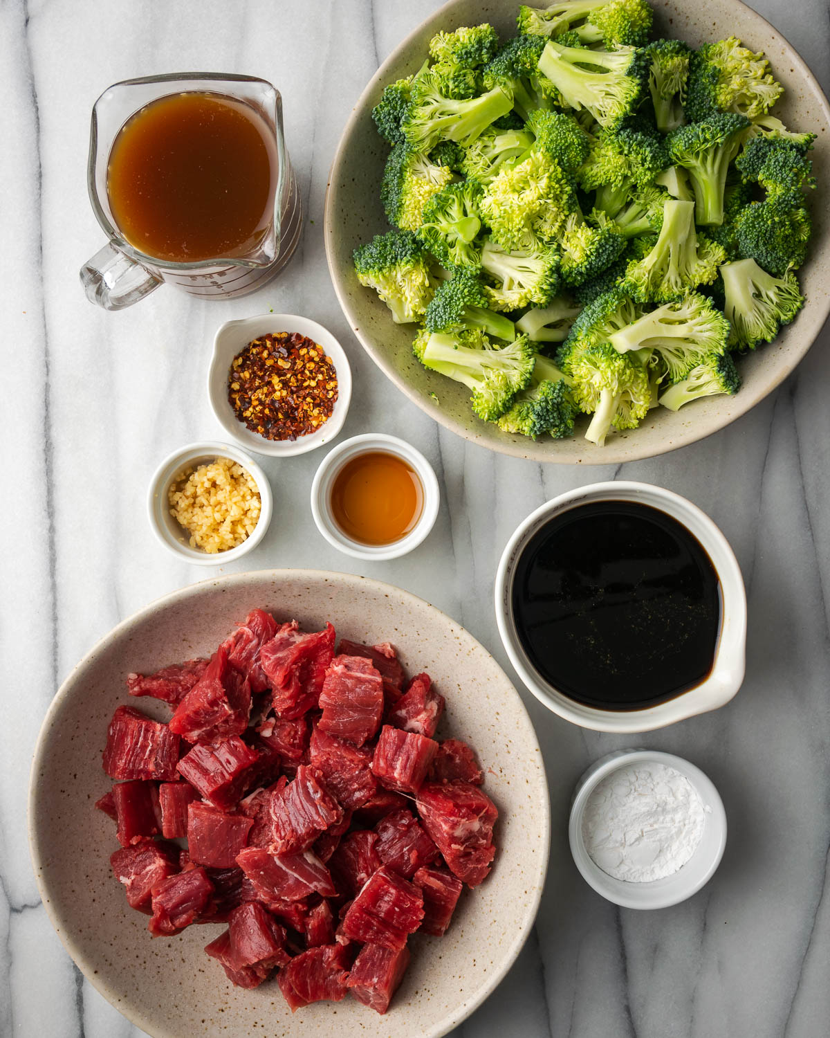 Ingredients for beef and broccoli on a white marble table.