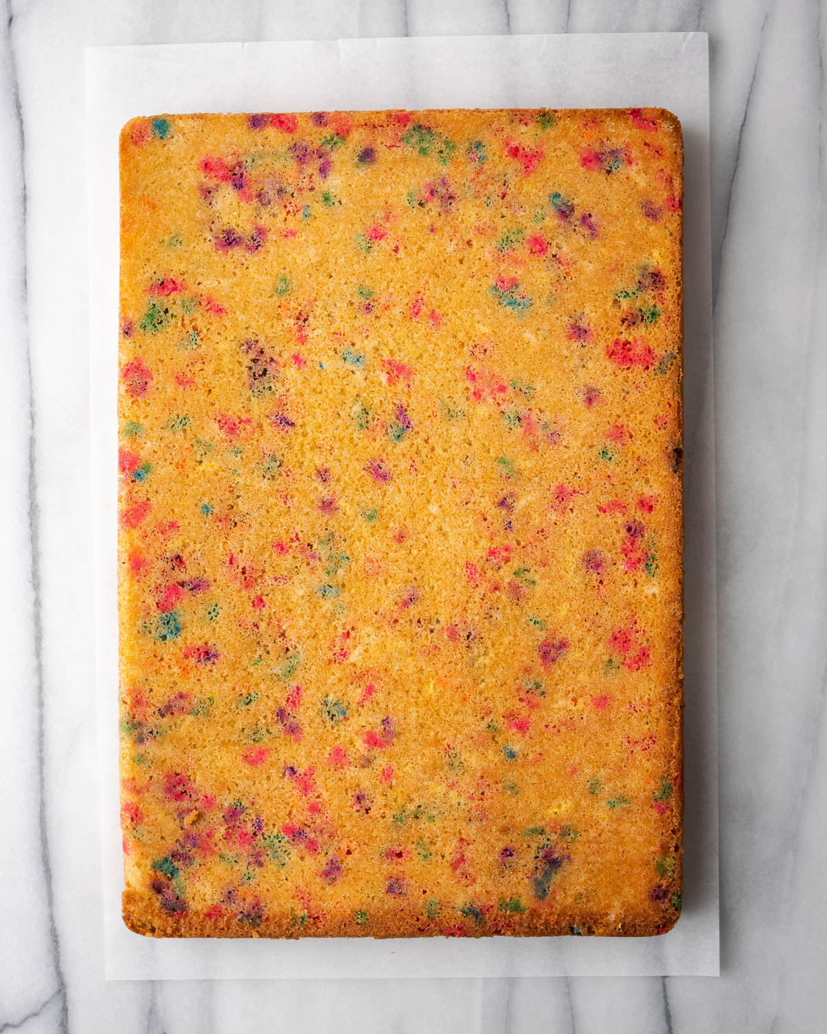 A funfetti sheet cake laid out on a piece of parchment paper.