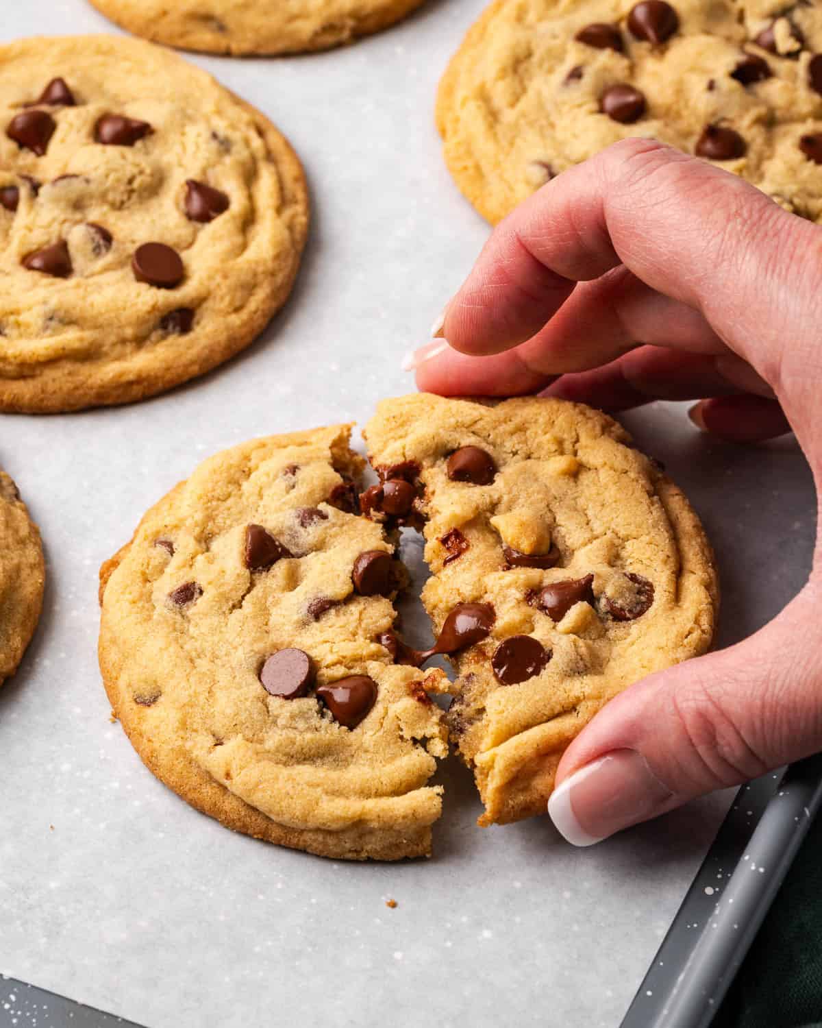 A hand grabbing half of a chocolate chip cookie showing all the melted chocolate inside.