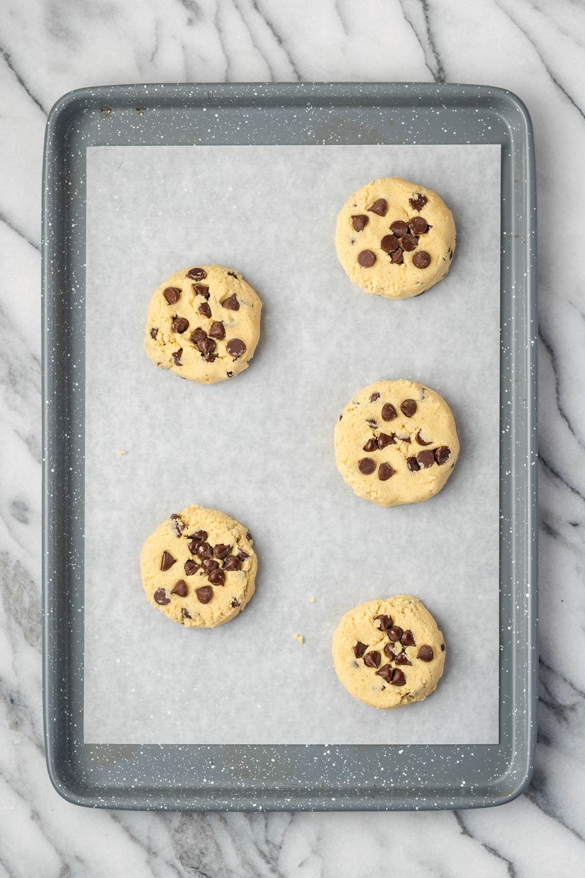 A baking sheet with 5 unbaked chocolate chip cookie dough balls. 