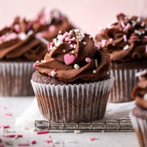 A gluten free chocolate cupcake topped with ganache frosting and pink and white sprinkles.