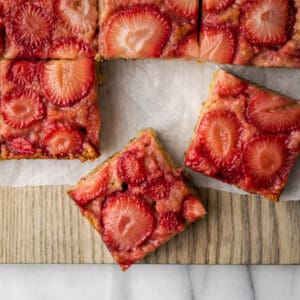 Squares of strawberry banana upside down cake on a wooden cutting board.