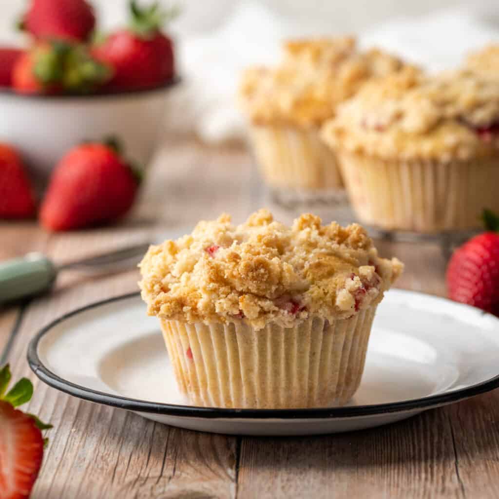 Gluten free strawberry muffin on a white plate sitting on a wooden table.