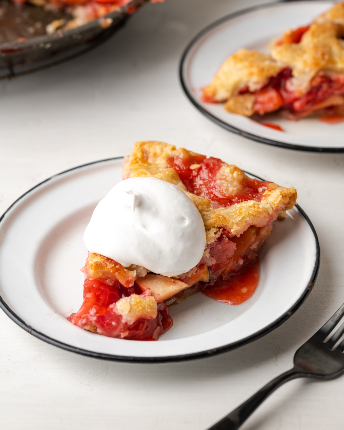 A slice of strawberry apple pie topped with whipped cream and served on a white plate.