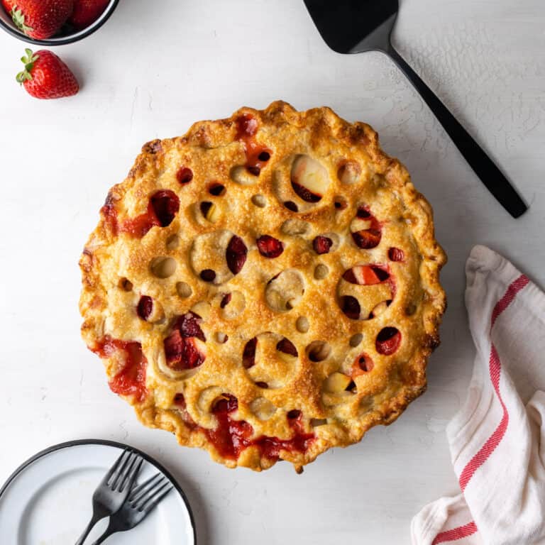 A strawberry apple pie sitting on a white table.