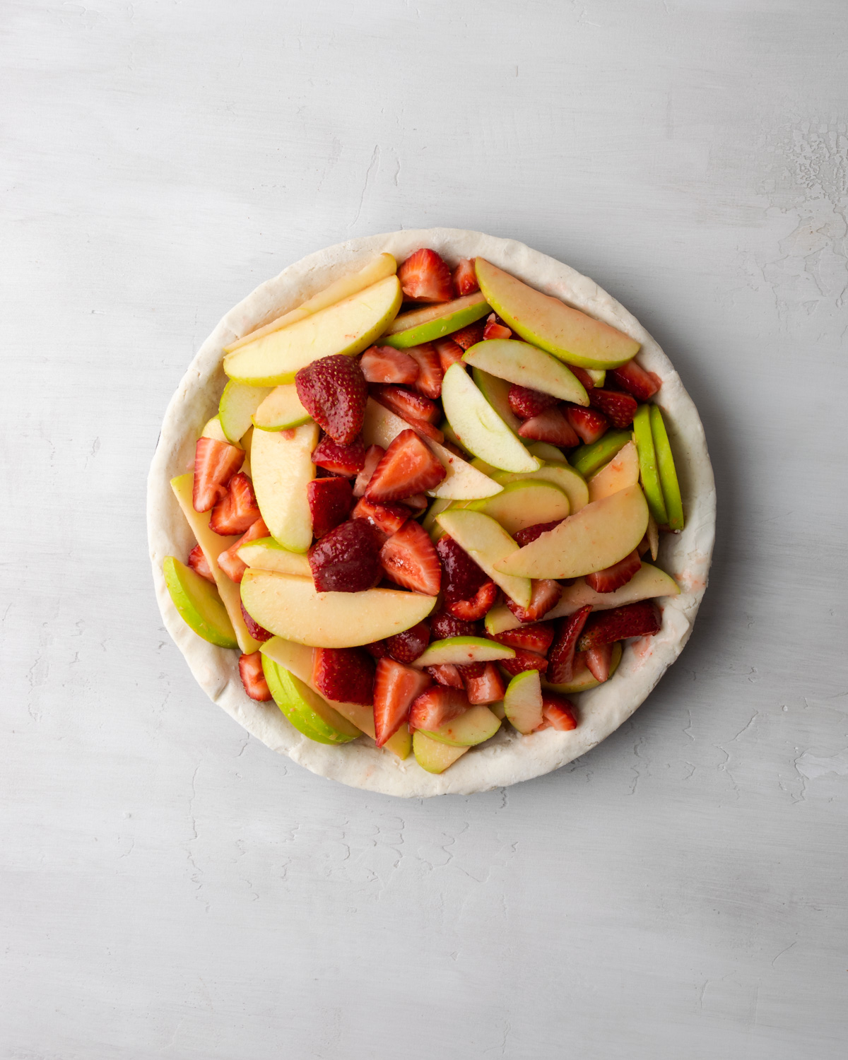 Apple and strawberry pie filling in an unbaked pie shell.