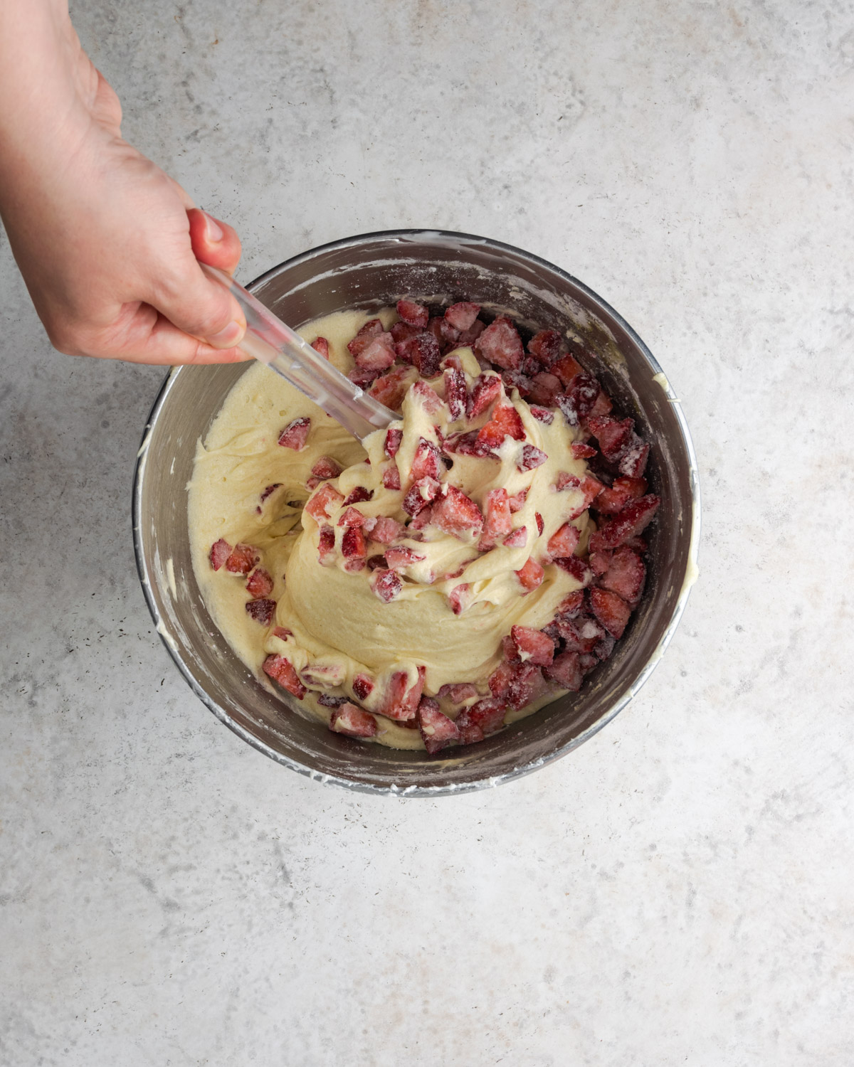 Strawberries being mixed into cake batter in a metal bowl.