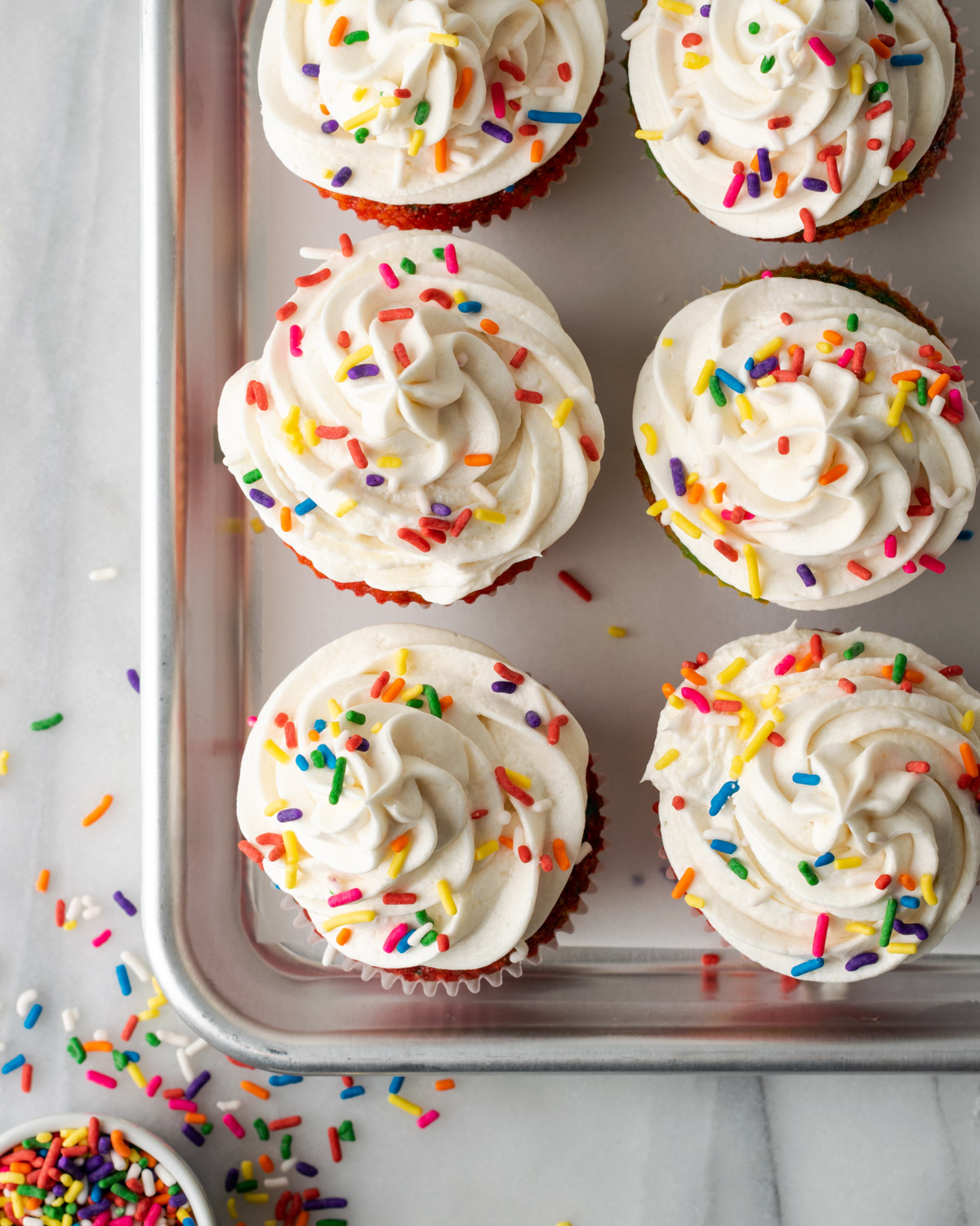 A batch of frosted cupcakes sitting on a metal baking tray.