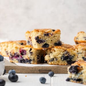 Three slices of gluten free blueberry cake stacked on a wooden cutting board.
