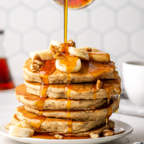 A stack of banana pancakes with maple syrup running down the sides.