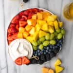 A fruit tray arranged in rainbow colors with a bowl of dairy free fruit dip.