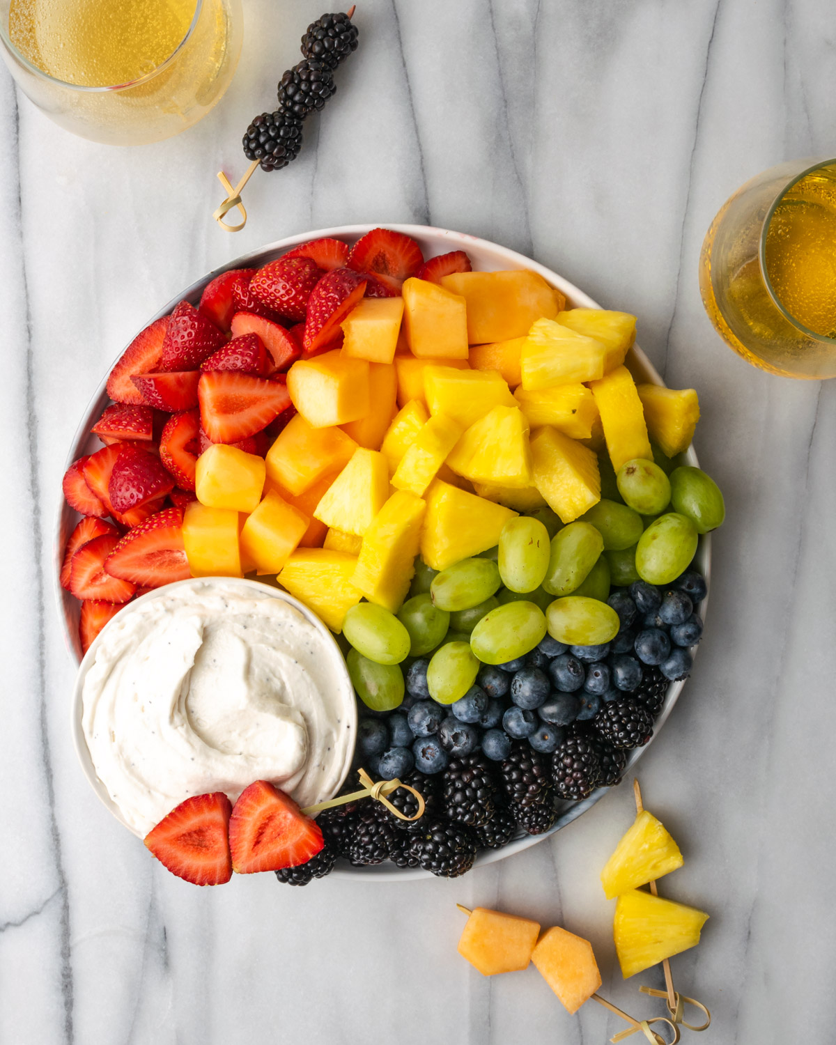 A rainbow fruit tray with a bowl of fruit dip.