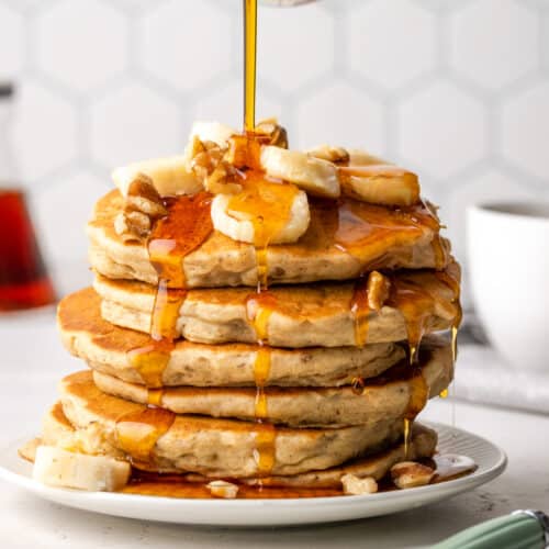 A stack of gluten free banana pancakes topped with sliced bananas and syrup.