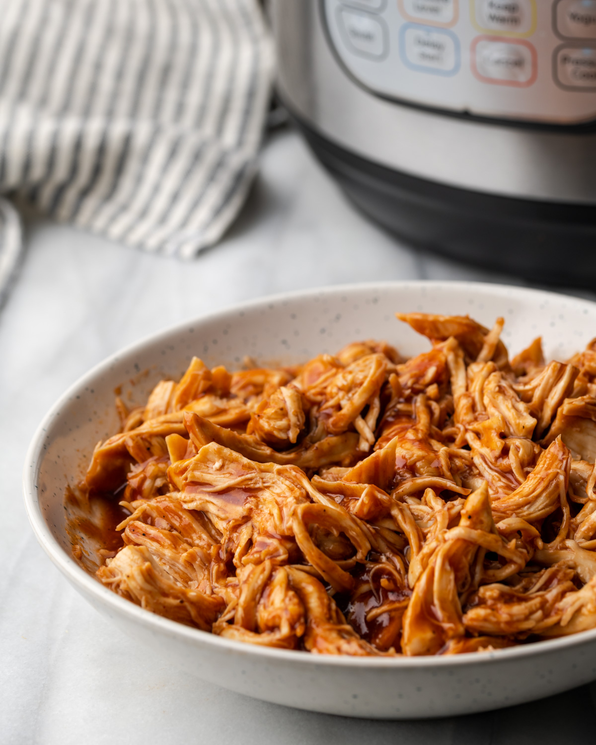 A bowl of pulled BBQ chicken on a white table.