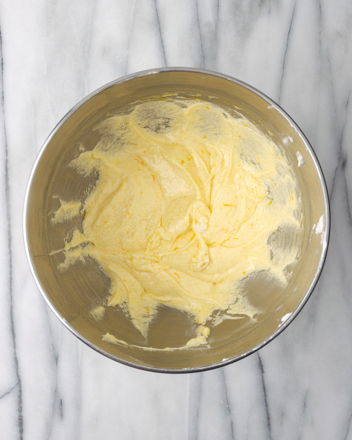 Partially mixed lemon loaf cake batter in a large metal mixing bowl.