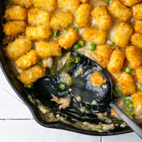 A cast iron skillet filled with chicken casserole with tater tots.