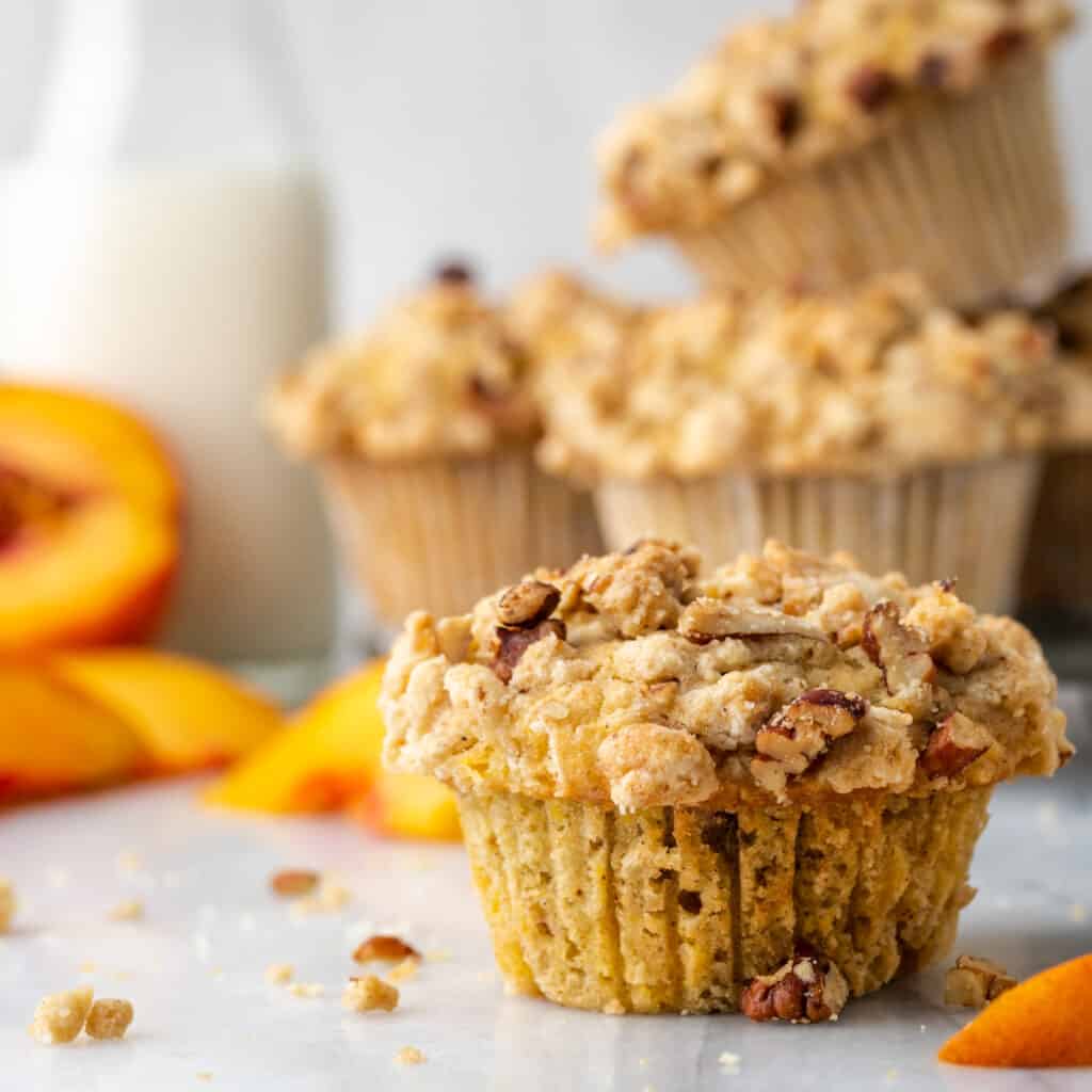 Gluten free peach muffins on a white table with a jar of milk.