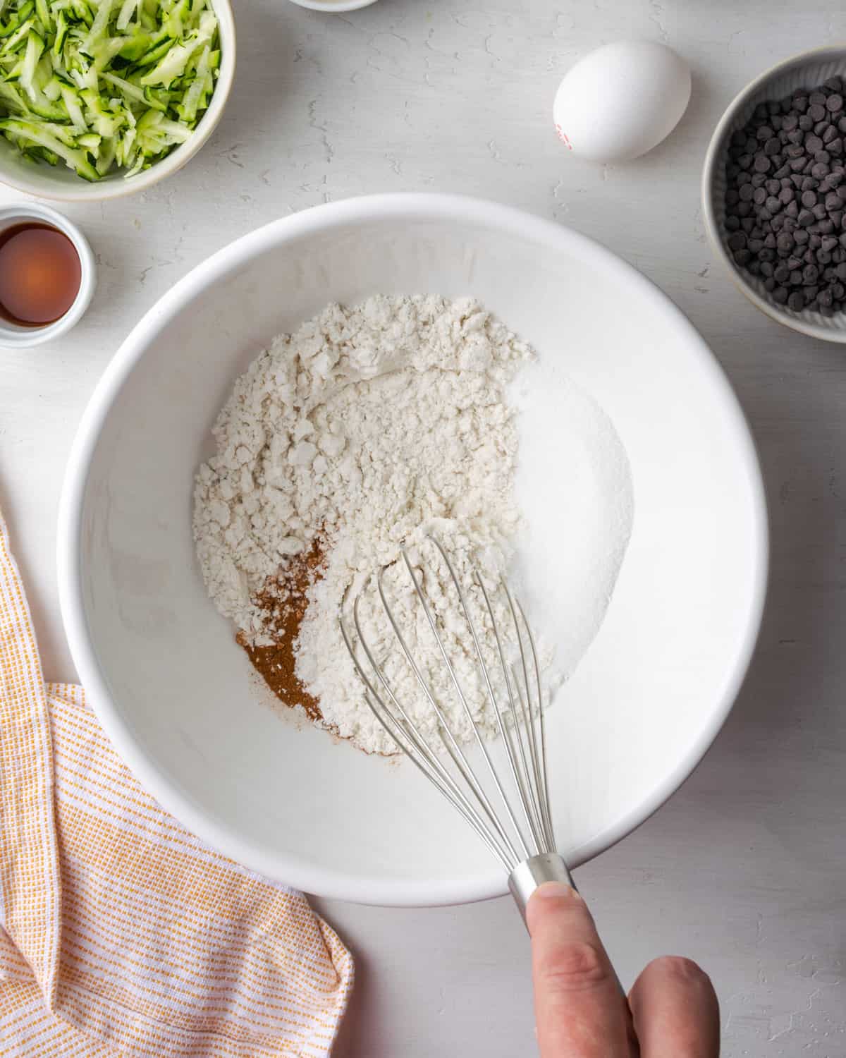 Gluten free flour, sugar, baking powder, salt and spices being whisked together in a large white bowl.