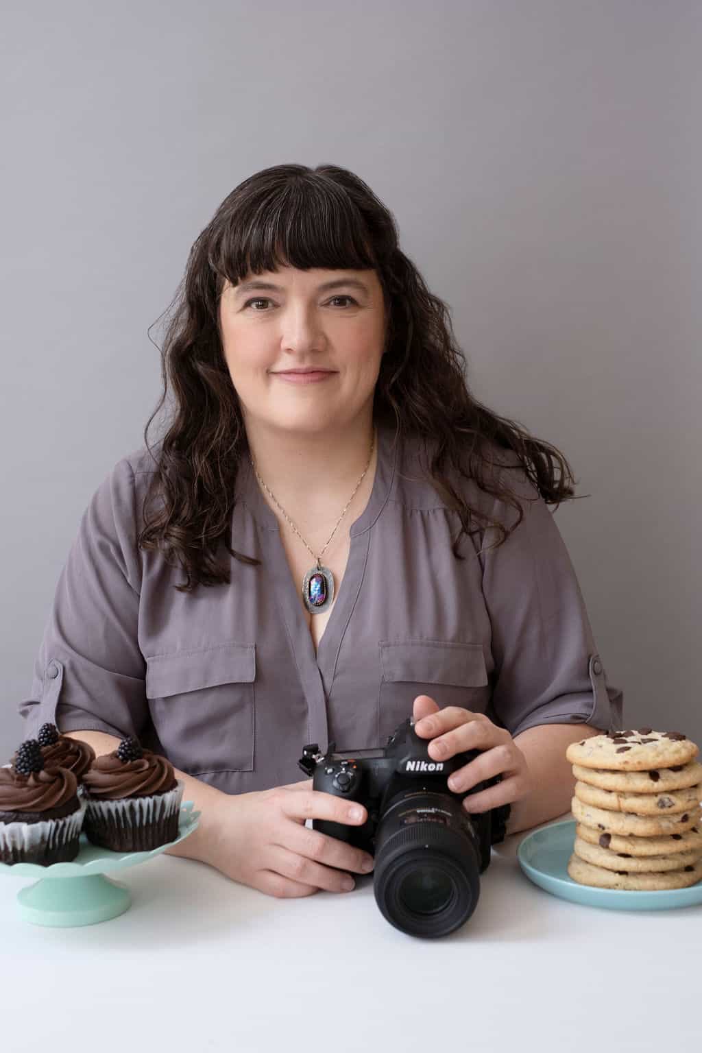 Photo of Tiffany Welsh holding a camera with plates of desserts.