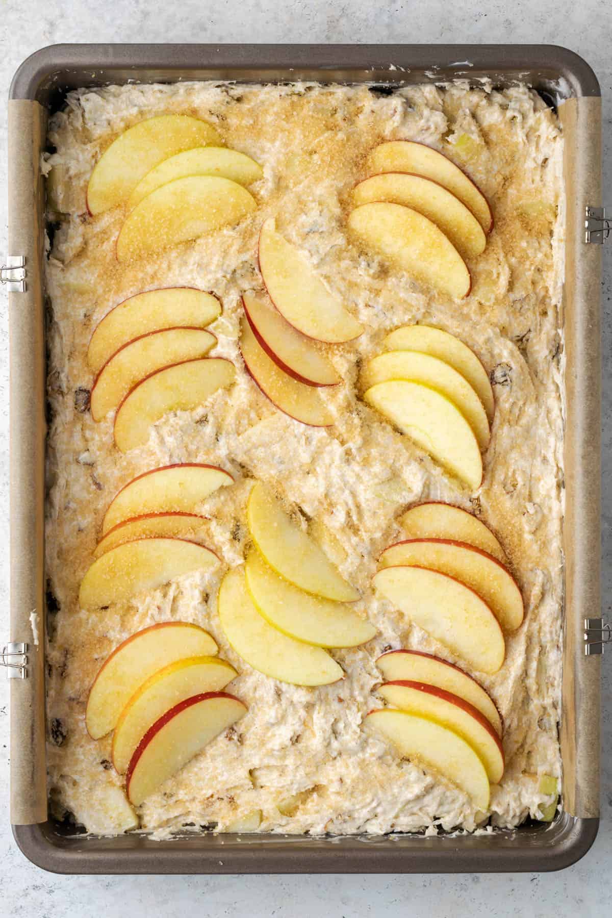 Unbaked gluten free apple cake in a 9x13 pan topped with slices of fresh apples.
