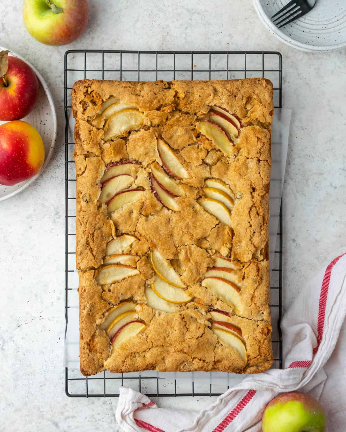A gluten free apple cake topped with fresh apple slices cooling on a wire rack.