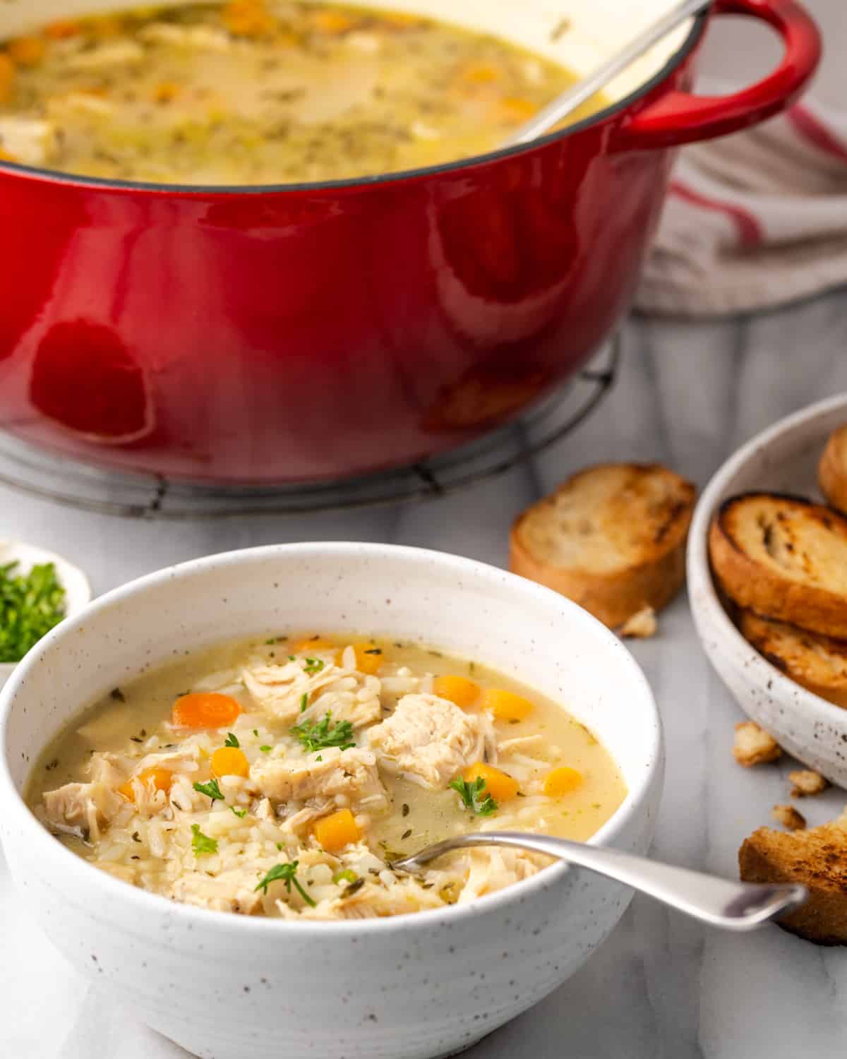 A bowl of chicken and rice soup served with toasted sliced bread.