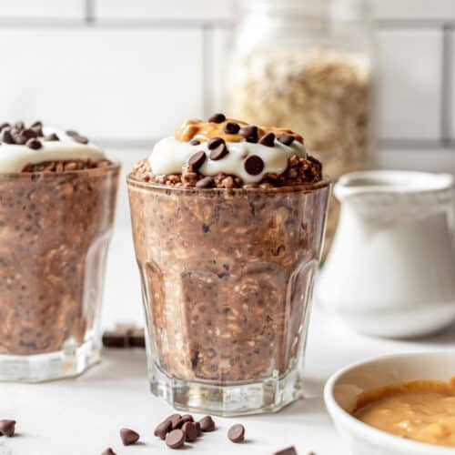 Two glasses filled with chocolate oatmeal and topped with yogurt and peanut butter.