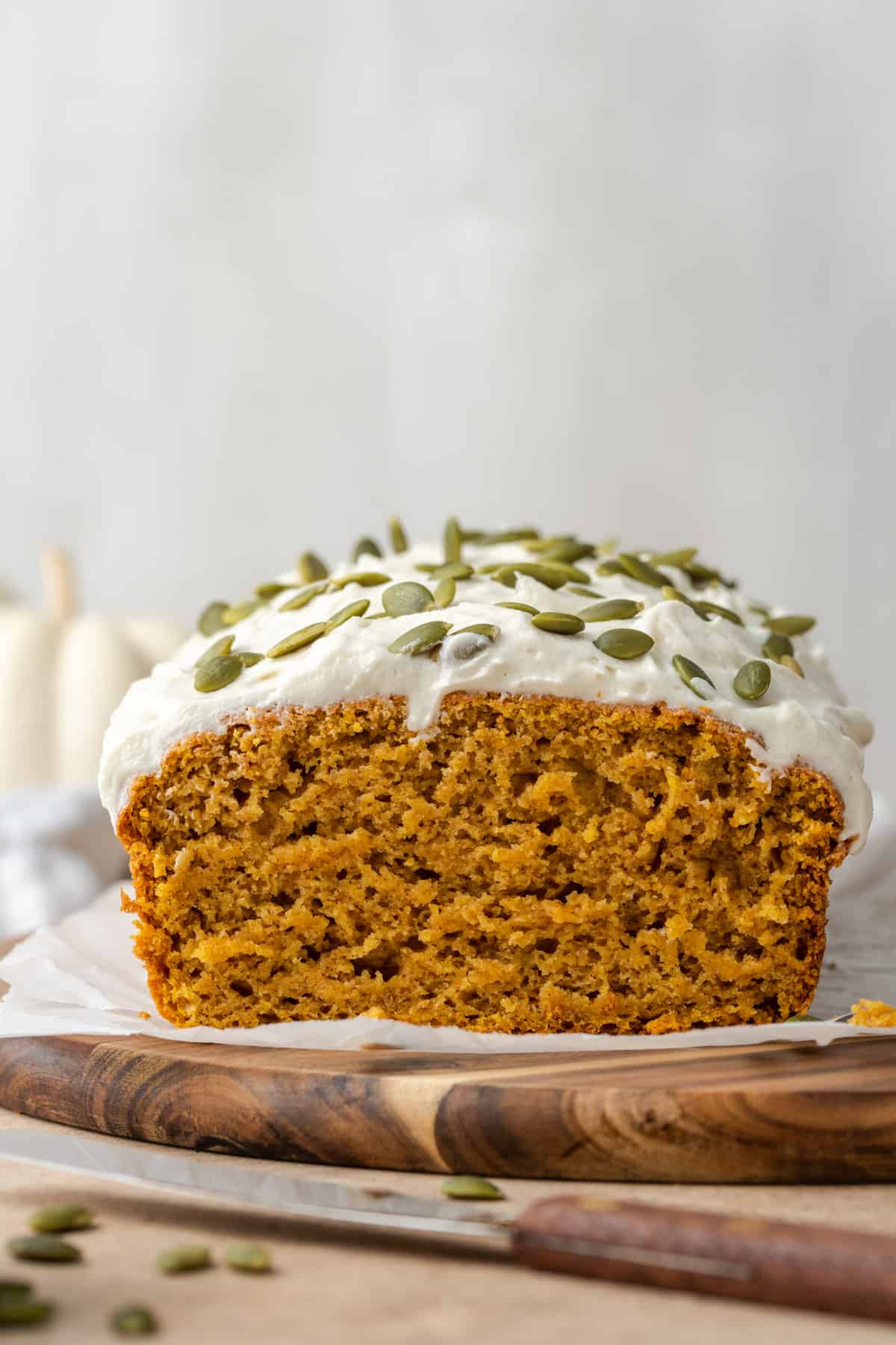 A closeup shot of pumpkin bread topped with cream cheese frosting and pepitas.