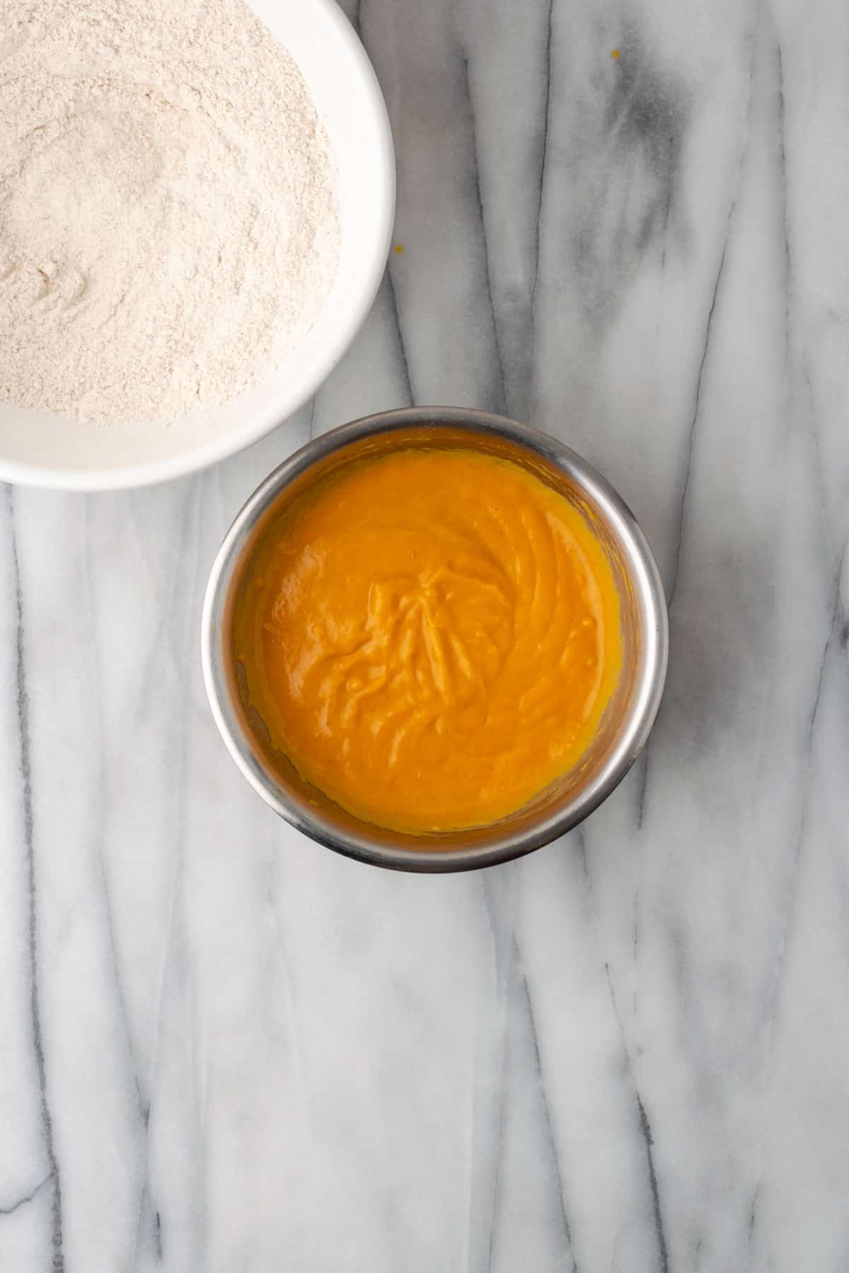 Pumpkin mixed with wet ingredients in a small metal bowl.