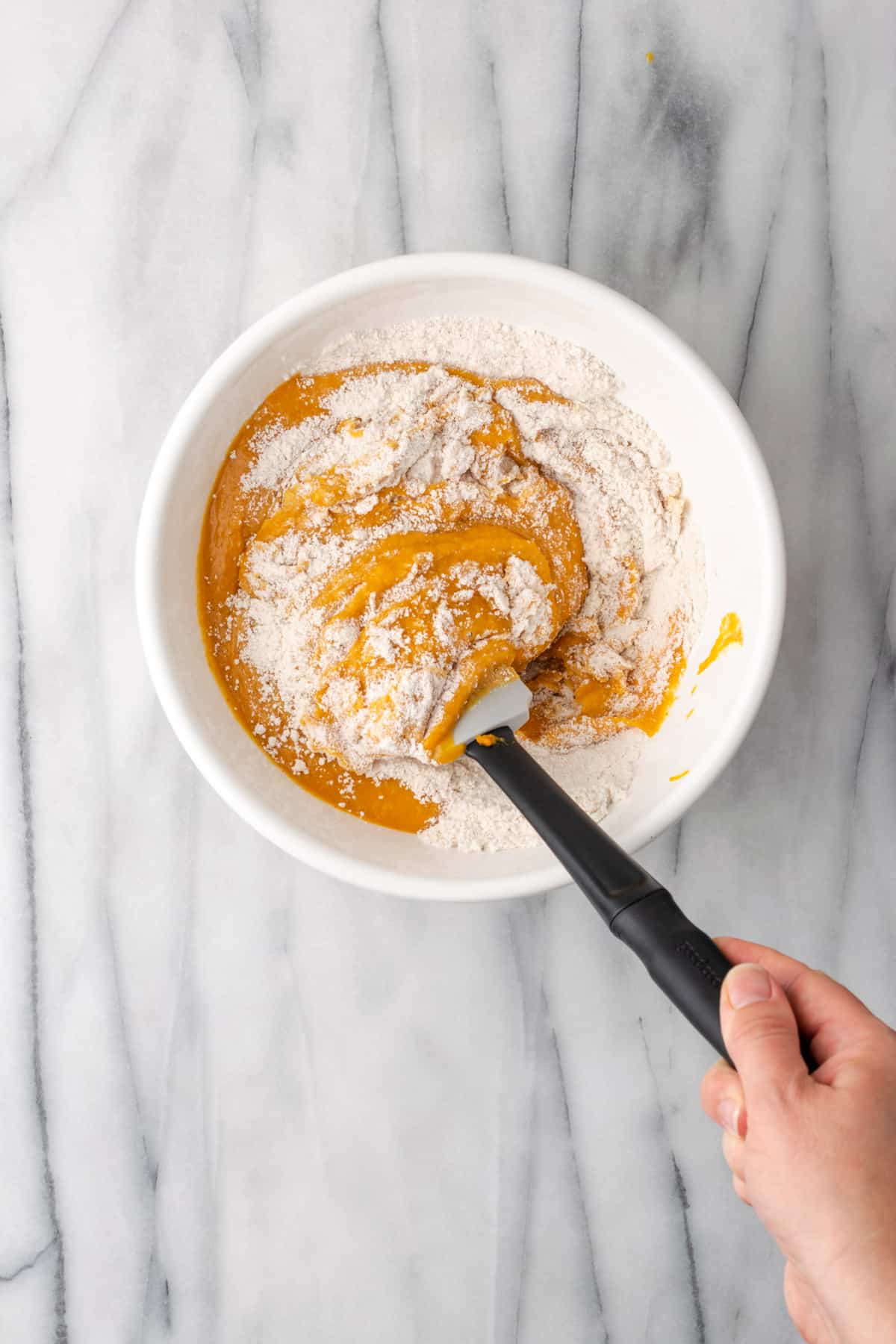 Wet and dry ingredients being folded together with a spatula.