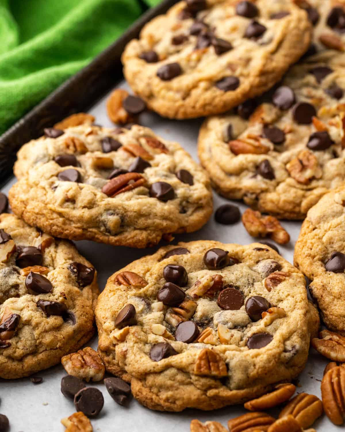 Closeup of chocolate chip cookies topped with pecans on a baking sheet.