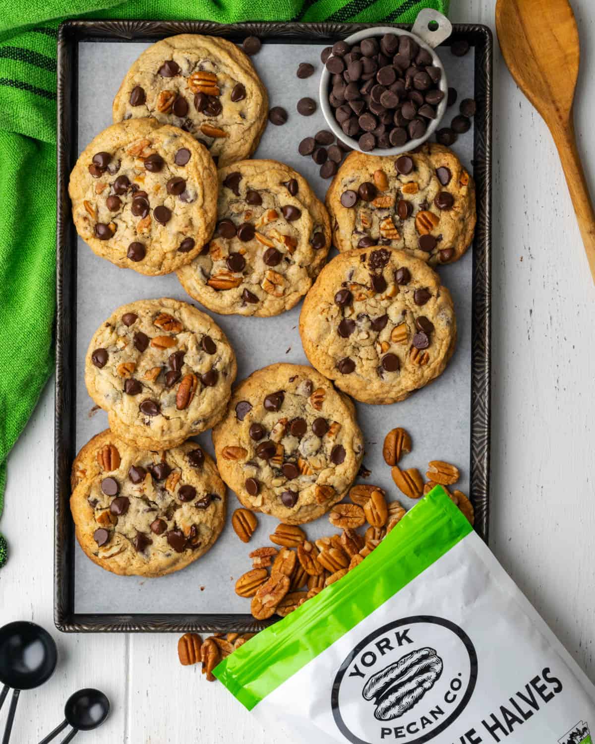 A pile of chocolate chip cookies with pecans on a metal baking sheet.