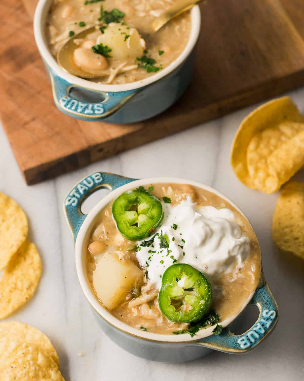 Two bowls of white chicken chili topped with sour cream and sliced jalapenos.