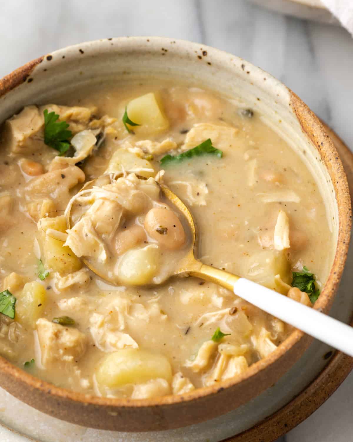 Closeup of a bowl of white chicken chili with beans, chicken and potato in a spoon.