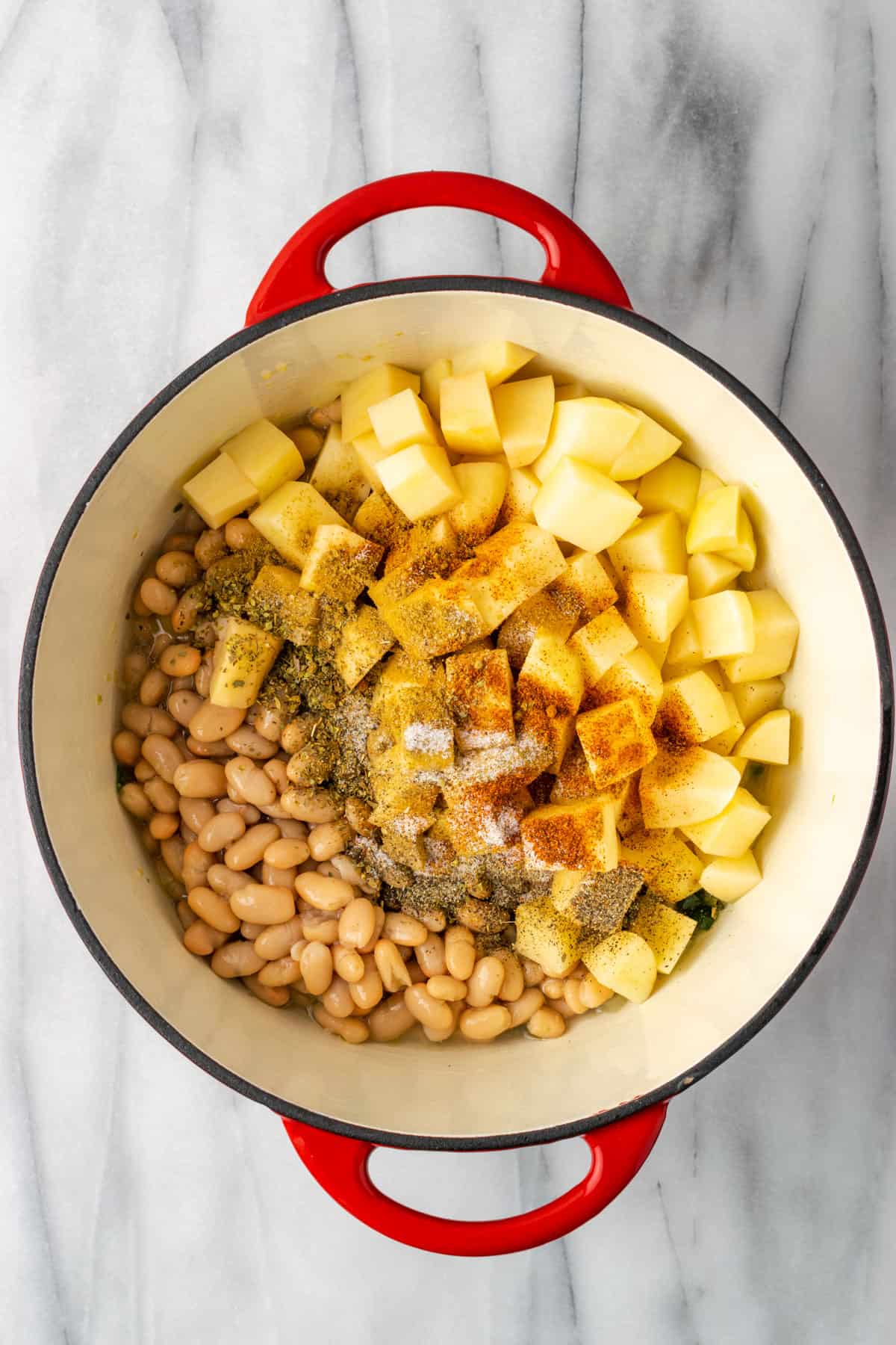 Beans, potatoes and seasoning added to sauteed vegetables in a dutch oven pot.