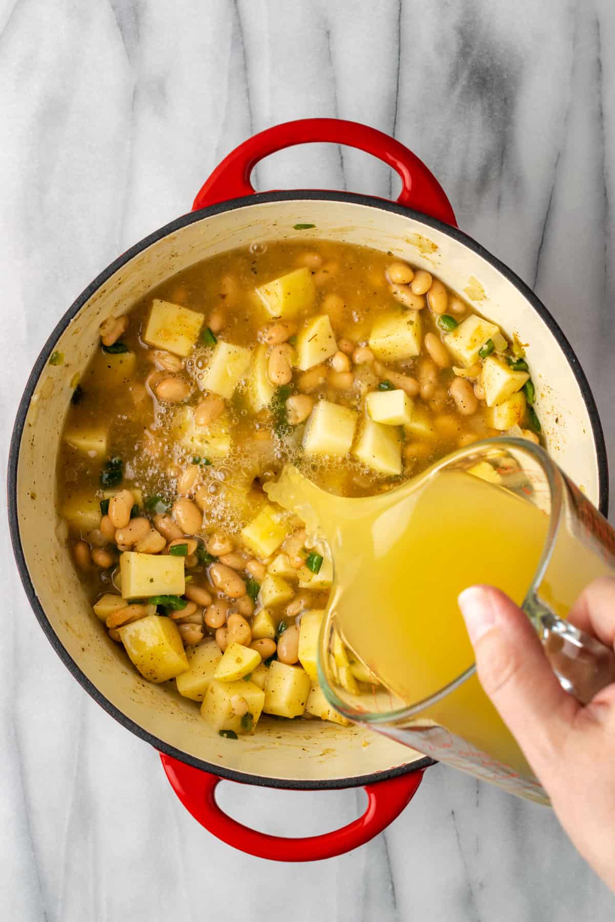 Chicken broth being poured into dutch oven pot.