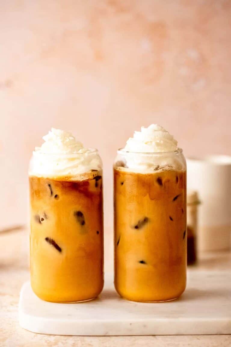 Two tall glasses of pumpkin chai latte topped with whipped cream.