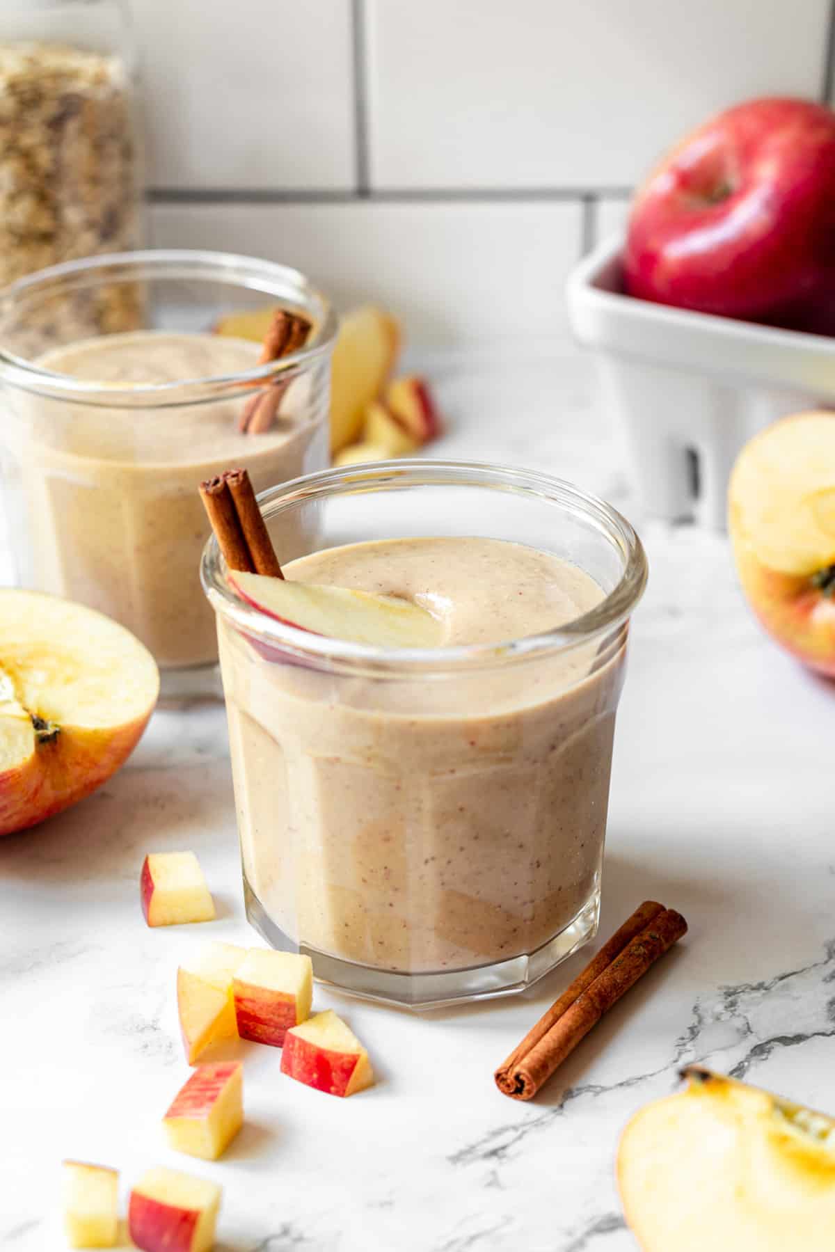 An apple and banana smoothie served in a small glass and garnished with a slice of apple and a cinnamon stick.