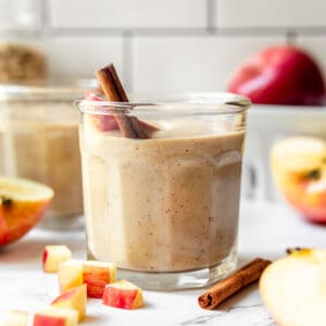 A small glass filled with apple banana smoothie and garnished with a cinnamon stick.