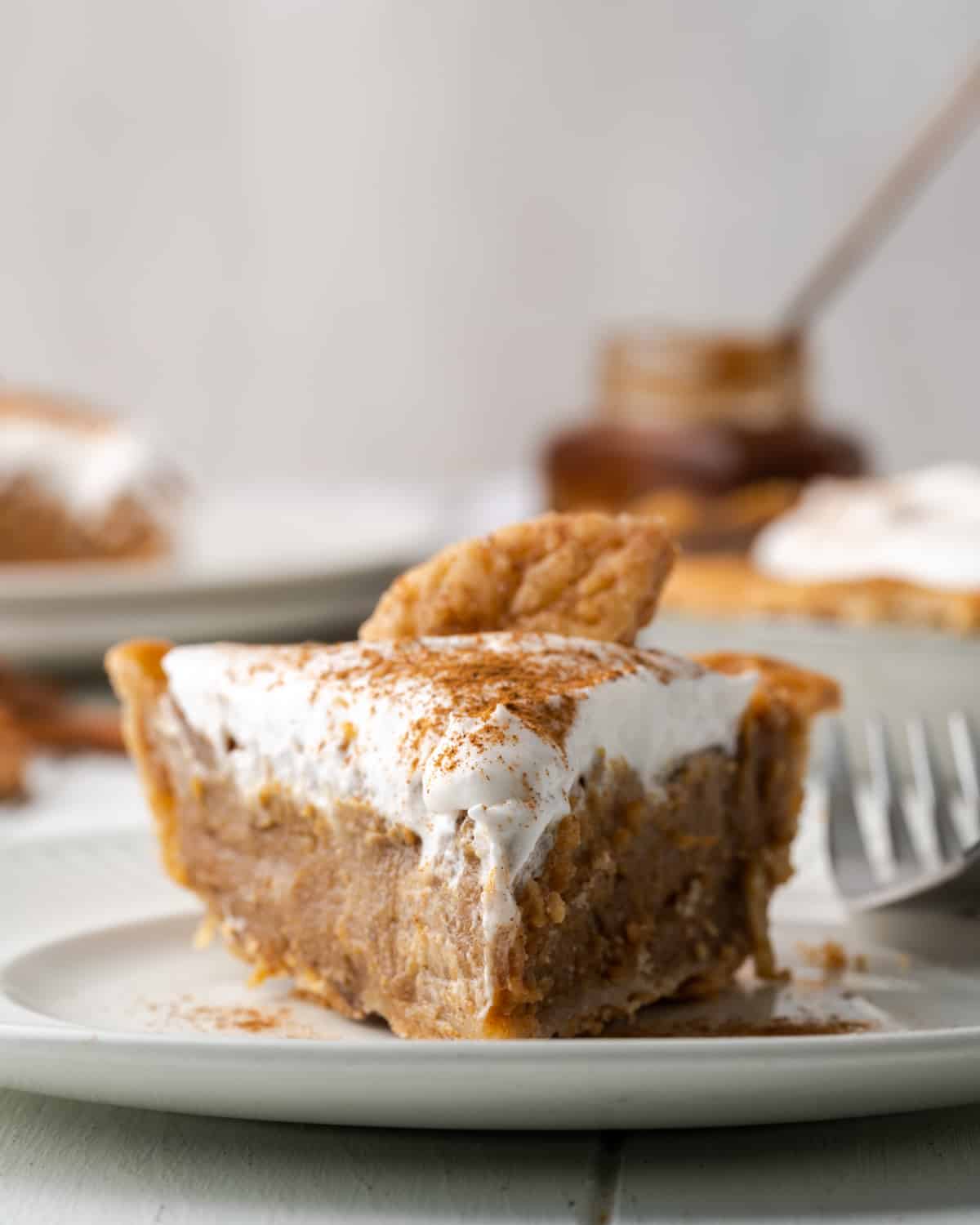 A closeup look at a slice of apple butter pie topped with whipped cream and a pie crust leaf.