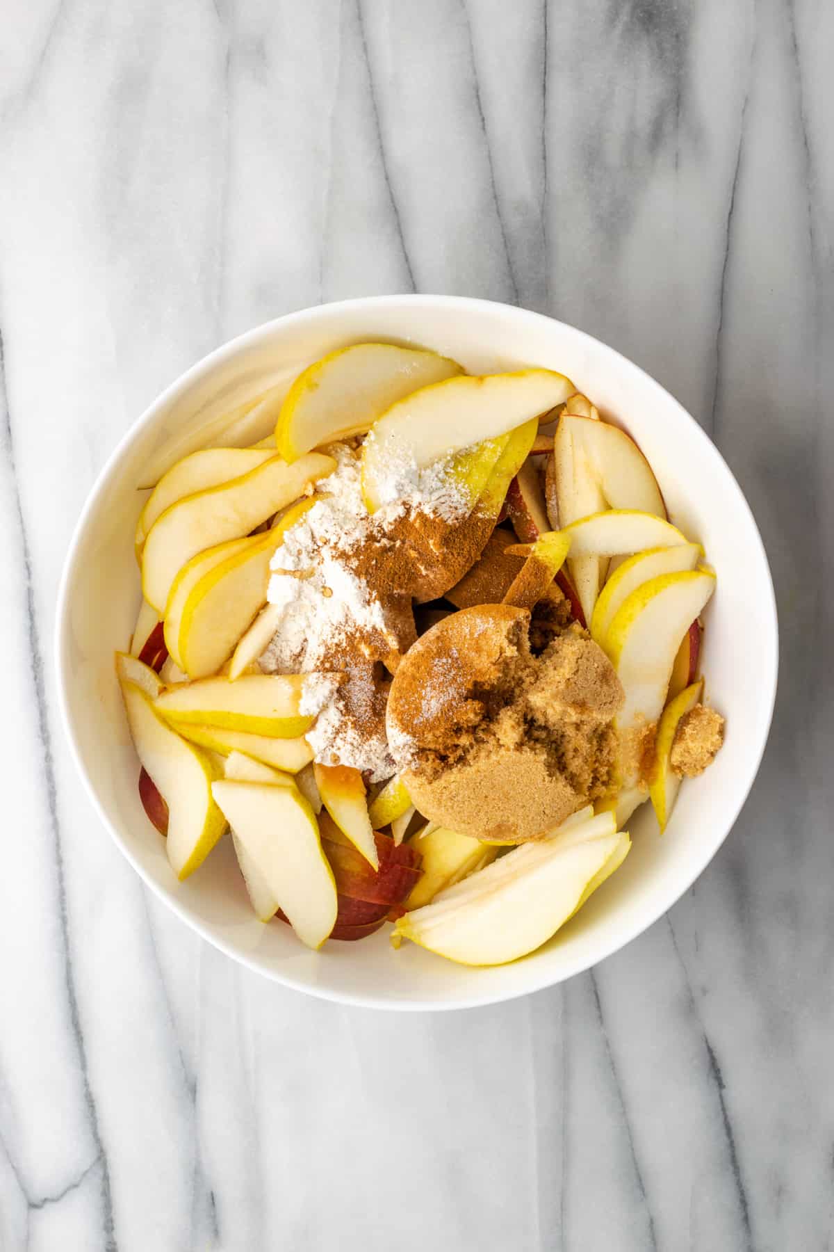 Ingredients for apple pear pie recipe in a white bowl.