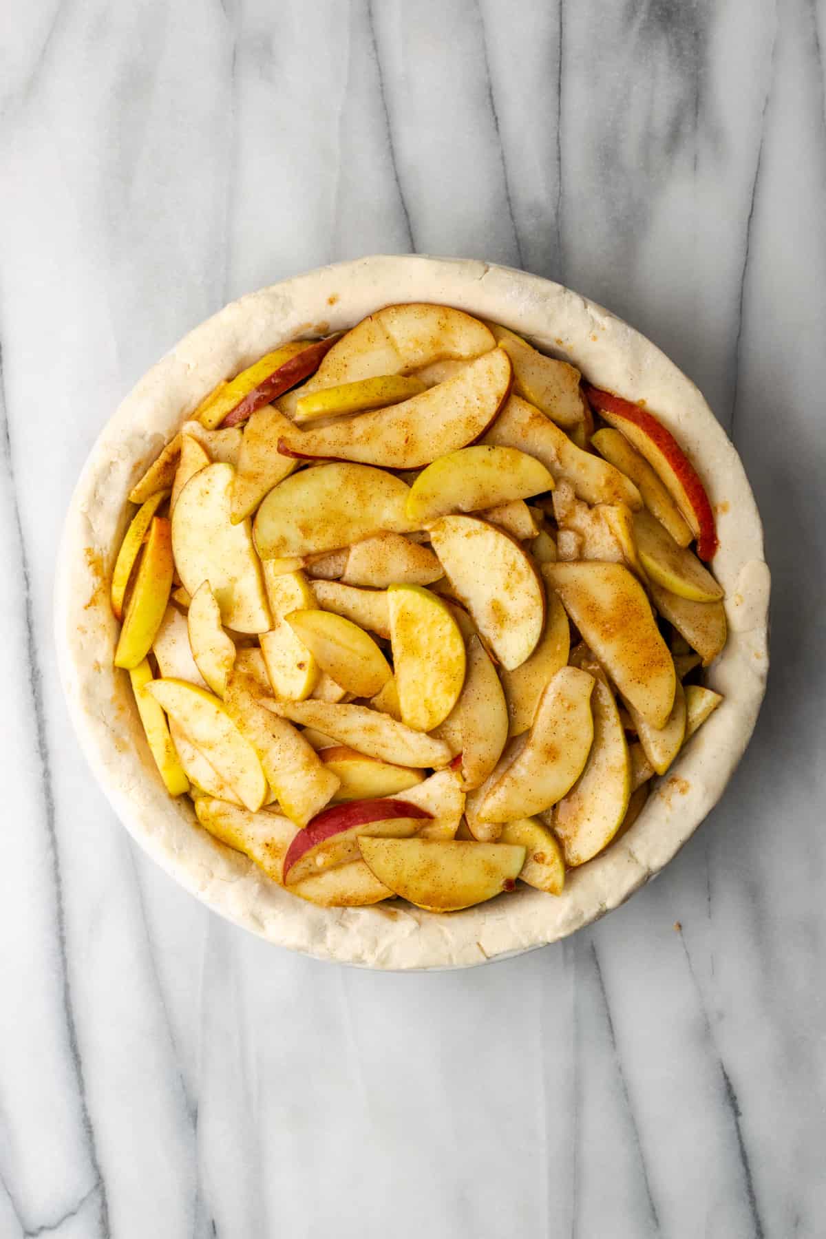 Apple pear pie filling in an unbaked pie shell on a marble table.