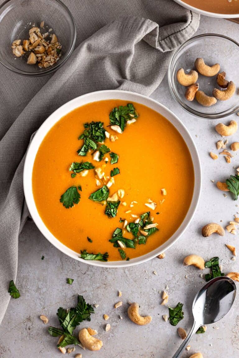 A bowl of cashew carrot ginger soup on a grey table.