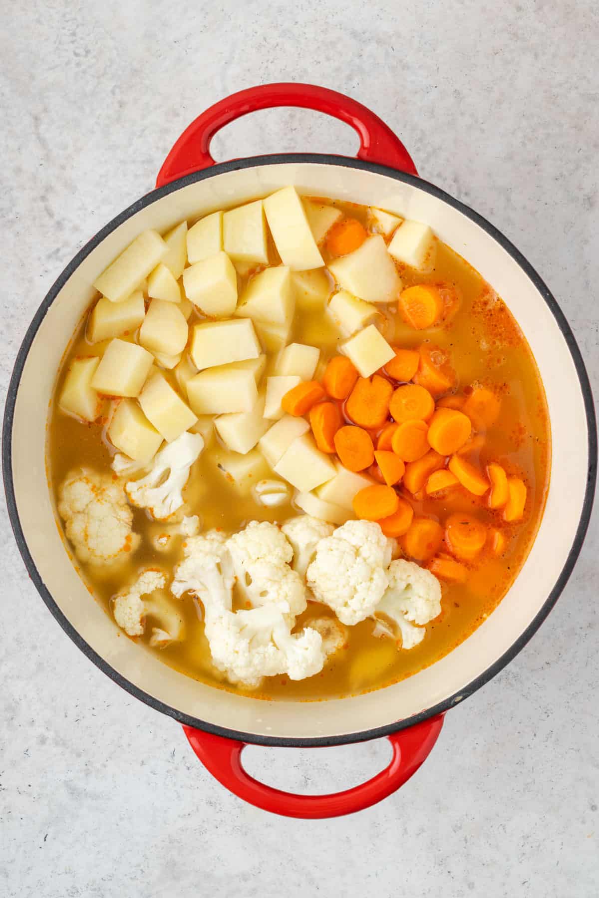 A soup pot filled with broth, potatoes, carrots and cauliflower.