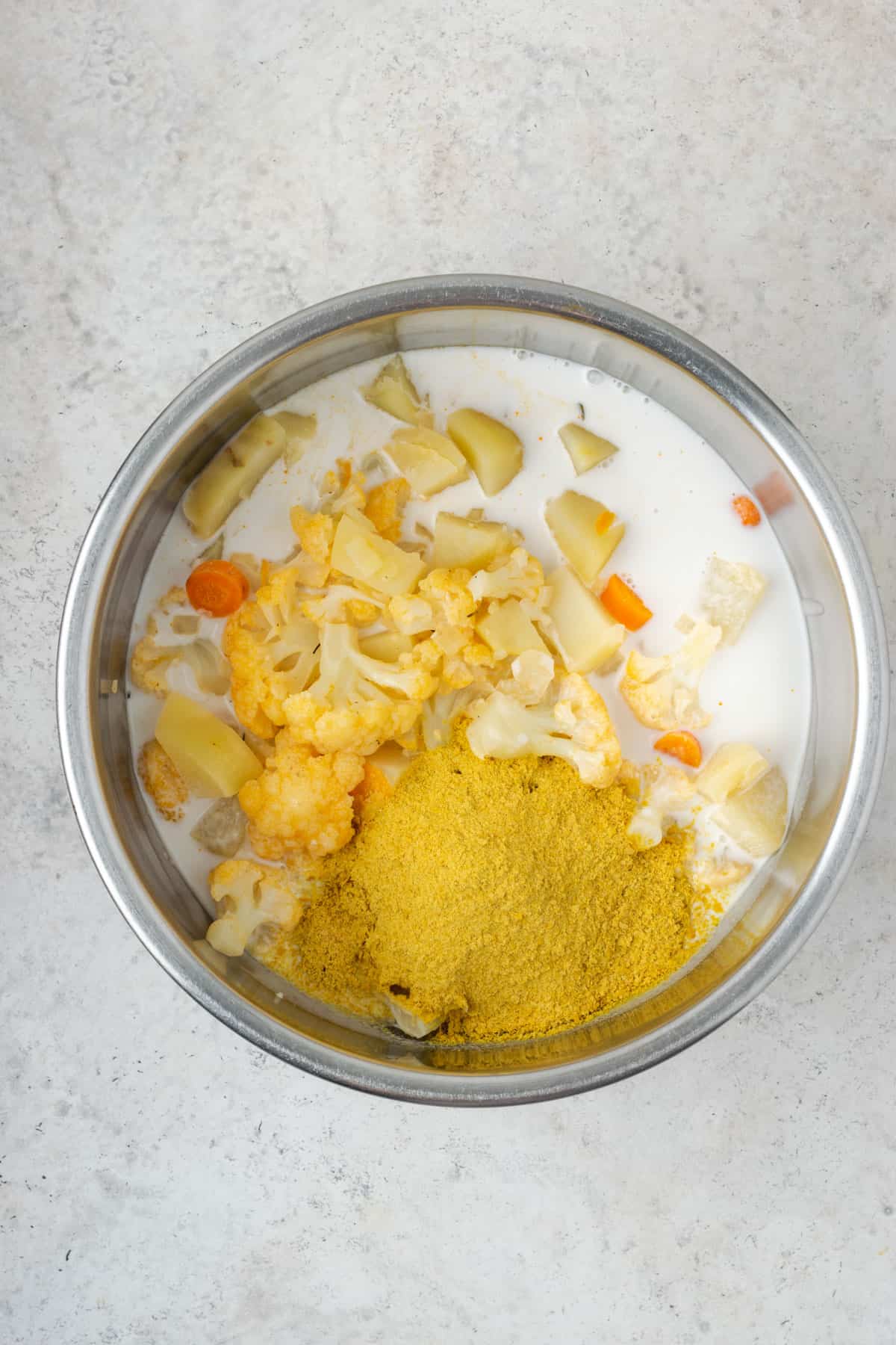 Cooked vegetables mixed with coconut milk and nutritional yeast in a metal bowl.