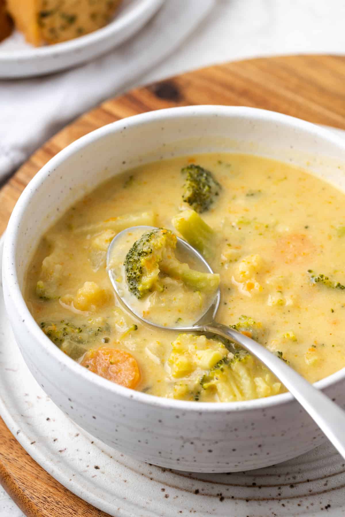 A bowl of broccoli cheese soup on a wood cutting board.