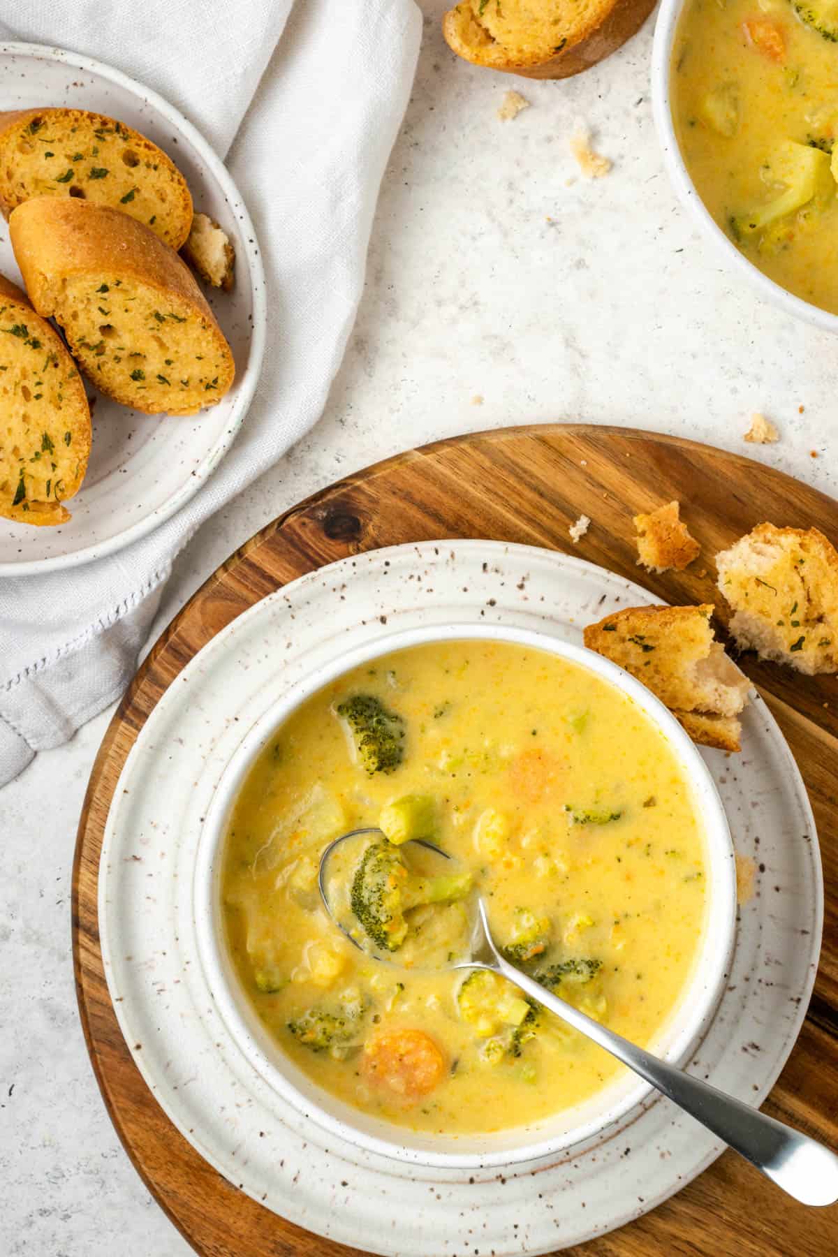 A bowl of broccoli cheese soup served with garlic bread on a white table.