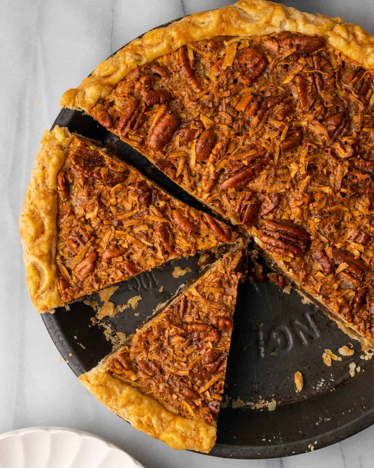 Overhead view of a sliced german chocolate pecan pie on a white marble table.