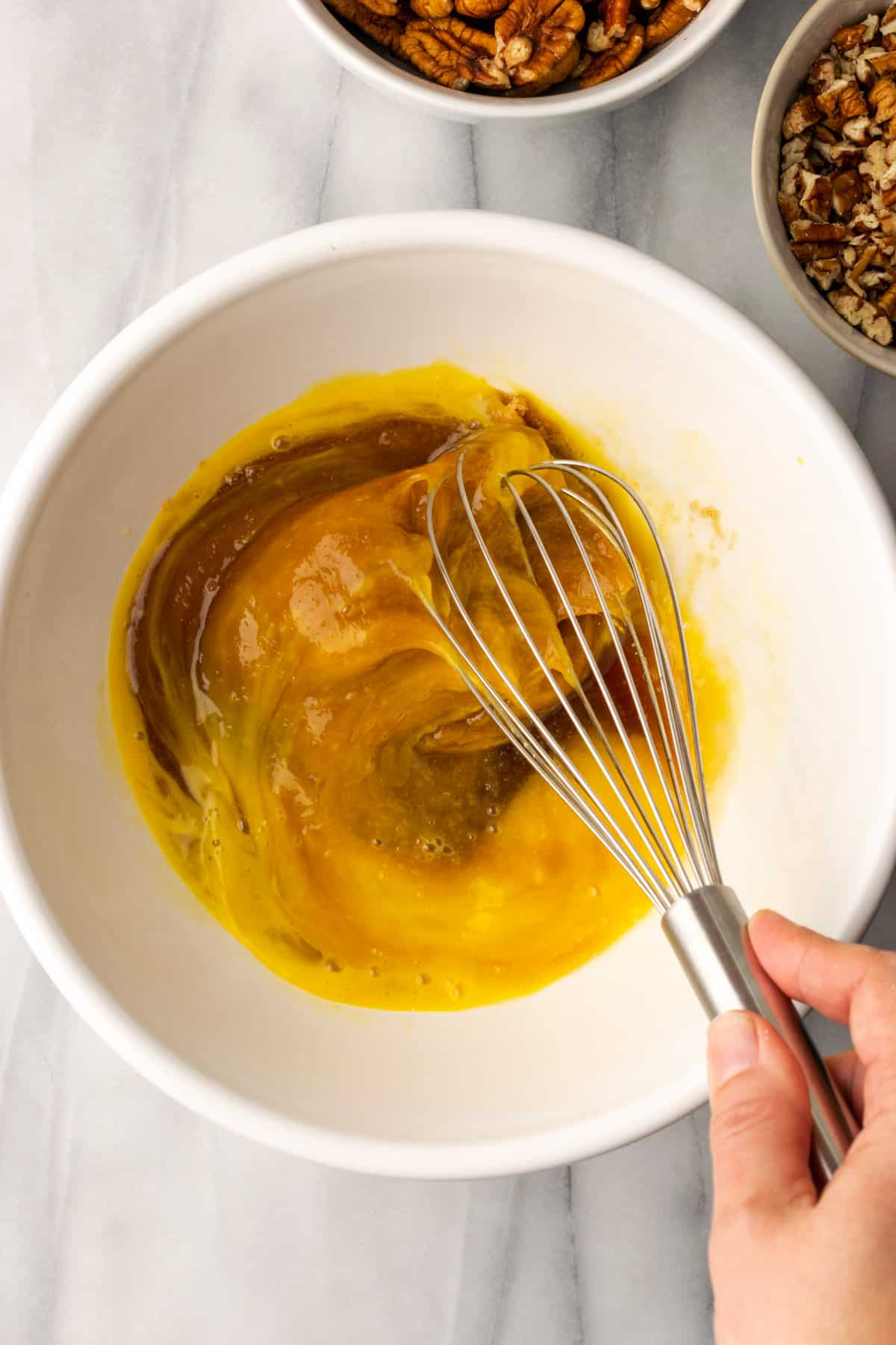 Pecan pie filling being whisked together in a large white bowl.