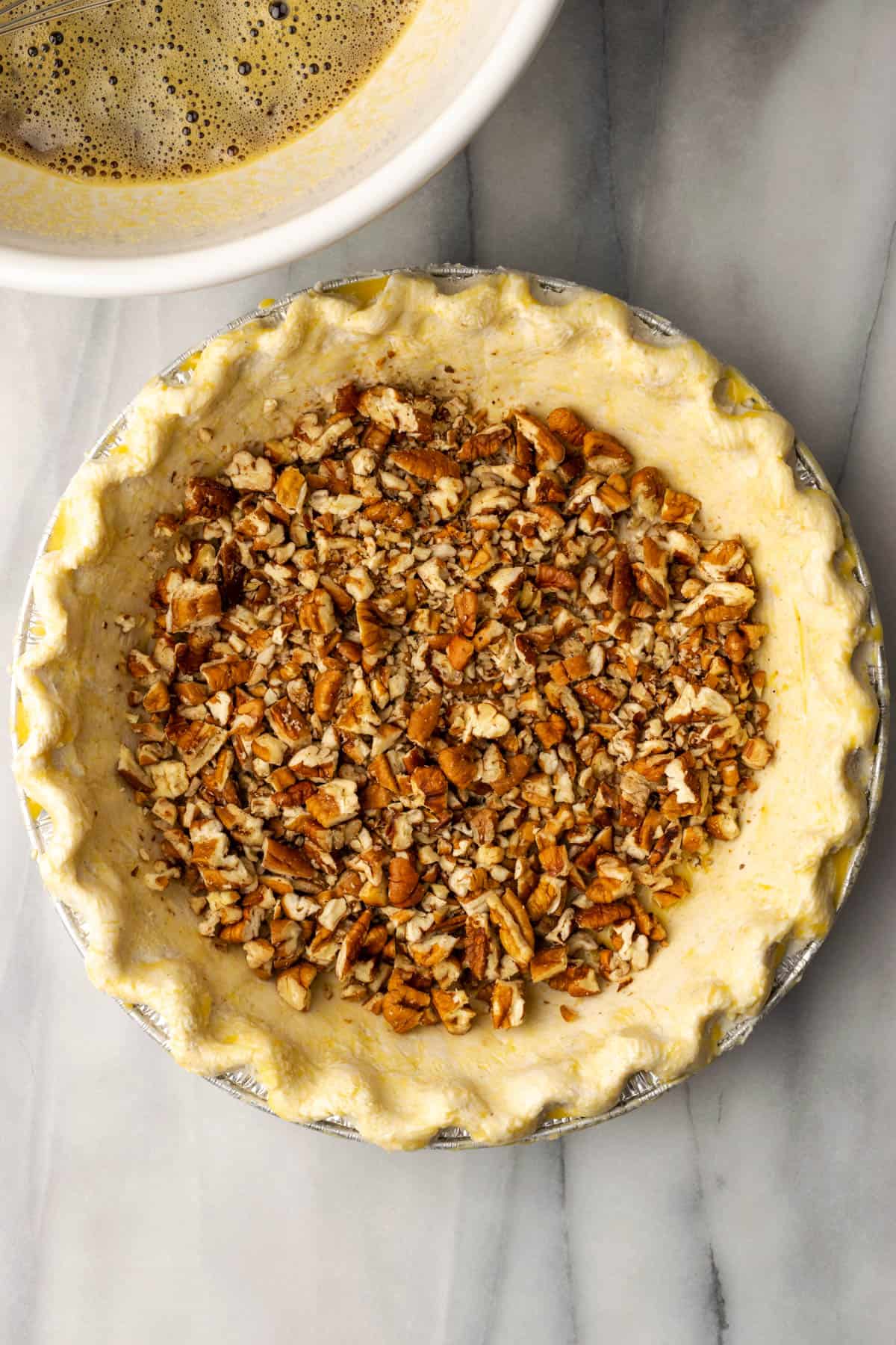 An unbaked pie shell filled with chopped pecan pieces.